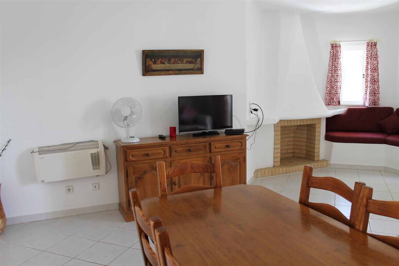 Una sala de estar con una mesa de comedor, muebles de madera, un televisor, una chimenea y un cuadro en la pared.
