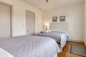 A hotel room with two beds, a bedside table with a lamp, a headboard, and two framed pictures on the wall.