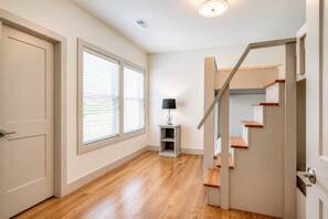 A hallway with a wooden floor, a door, and a staircase with a light fixture above.