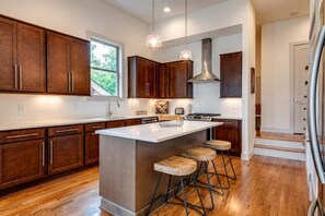 Une cuisine moderne avec des meubles en bois foncé, un grand îlot central doté de tabourets, des appareils en acier inoxydable et un éclairage suspendu.