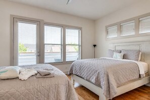 A bedroom with two beds, a large window with blinds, and a floor lamp.