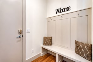 A reception area with a 'Welcome' sign, a bench with two patterned cushions, and a door with a blue handle.