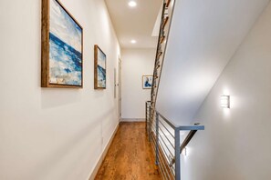 A hallway with wooden flooring, white walls, and a staircase with metal railings. - Nashville Getaway • Walk to Broadway & Vandy (Nashville)