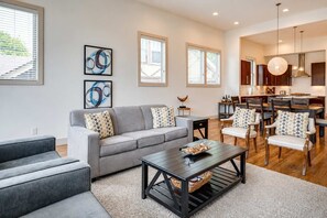 A modern living room with a grey sofa, matching armchairs, a coffee table, and a dining area with wooden chairs and a table.