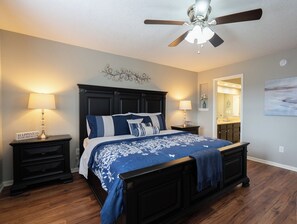 A bedroom with a large bed, two bedside tables, a ceiling fan, and a nightstand with a lamp.