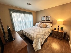 A hotel room with a bed, a desk, a nightstand, a lamp, and a window with curtains.