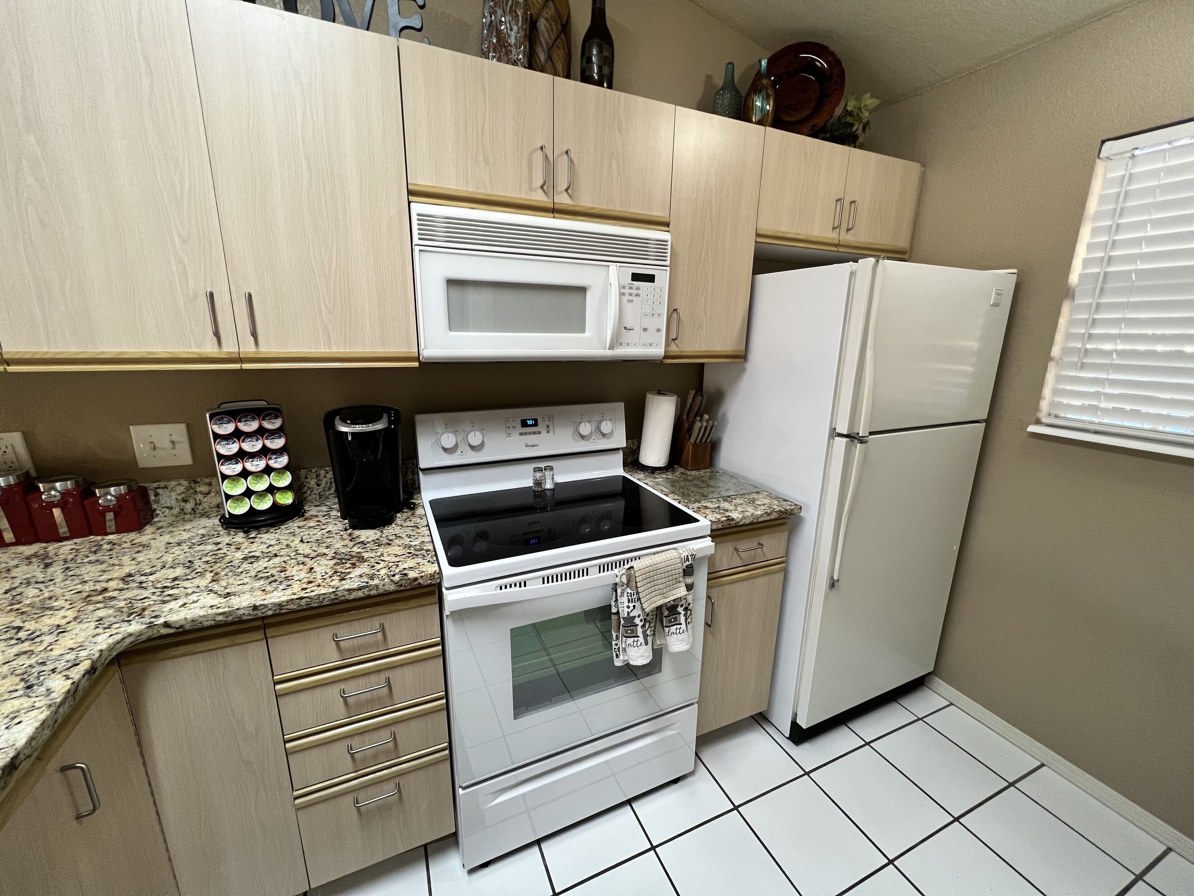 A kitchen with light wooden cabinets, a white microwave, a stove, a refrigerator, and a coffee maker.