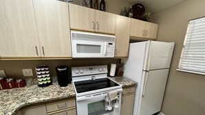A kitchen with light wooden cabinets, a white microwave, a stove, a refrigerator, and a coffee maker.