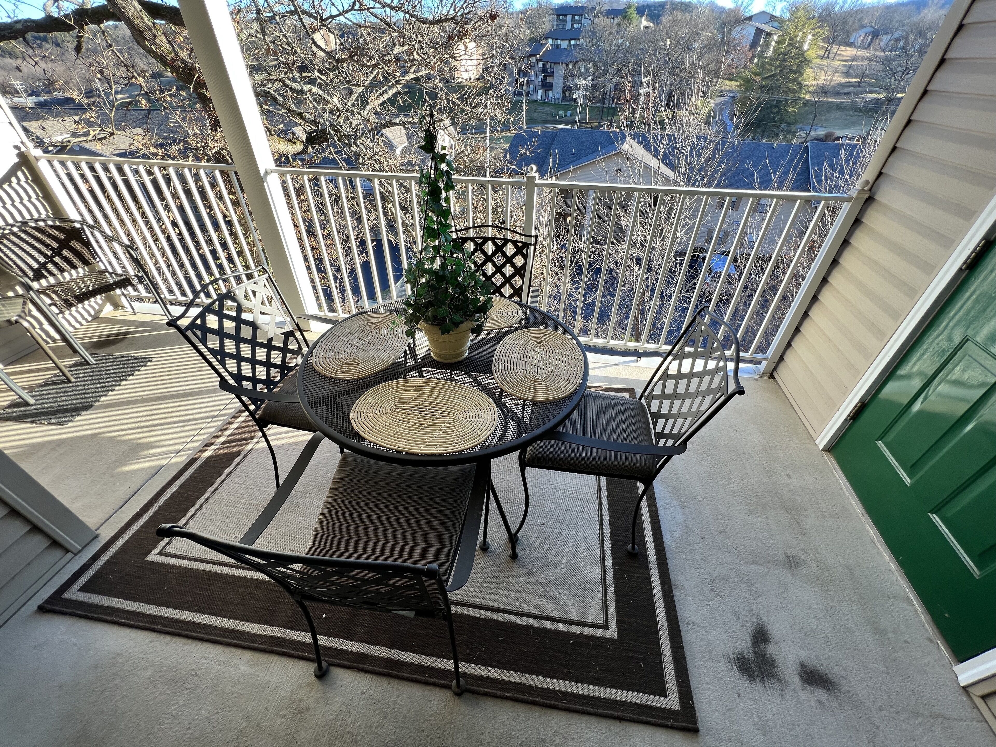 A balcony with a table and chairs, a potted plant, and a view of a residential area.