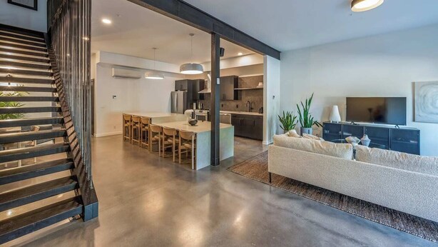 A modern living space with a staircase, a kitchen, and a seating area with a TV.