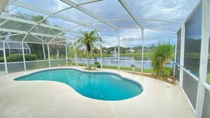 Una piscina techada con borde curvo, rodeada por una valla blanca, con vista a un cuerpo de agua y vegetación.