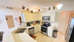 Una cocina moderna con gabinetes blancos, microondas, estufa, lavavajillas y refrigerador.
