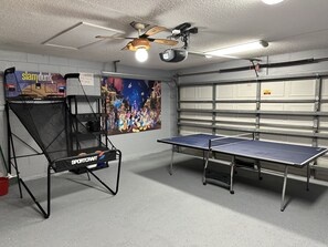 A ping pong table, a ceiling fan, and a poster on a wall.