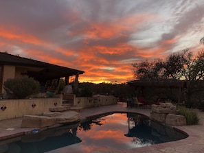 A pool with a stone edge, surrounded by a patio area with outdoor furniture and a covered seating area.