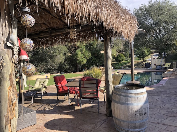 A patio area with a pool, red chairs, a wooden barrel, and hanging decorative lights.