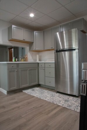 A modern kitchen with grey cabinets, a stainless steel refrigerator, and a patterned rug.