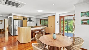 A modern kitchen with a central island, stainless steel appliances, and a dining area with wicker chairs and a wooden table.