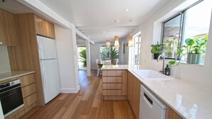 Eine moderne Küche mit Holzausstattung, einem weißen Kühlschrank, einem Geschirrspüler und einem großen Fenster mit Pflanzen.