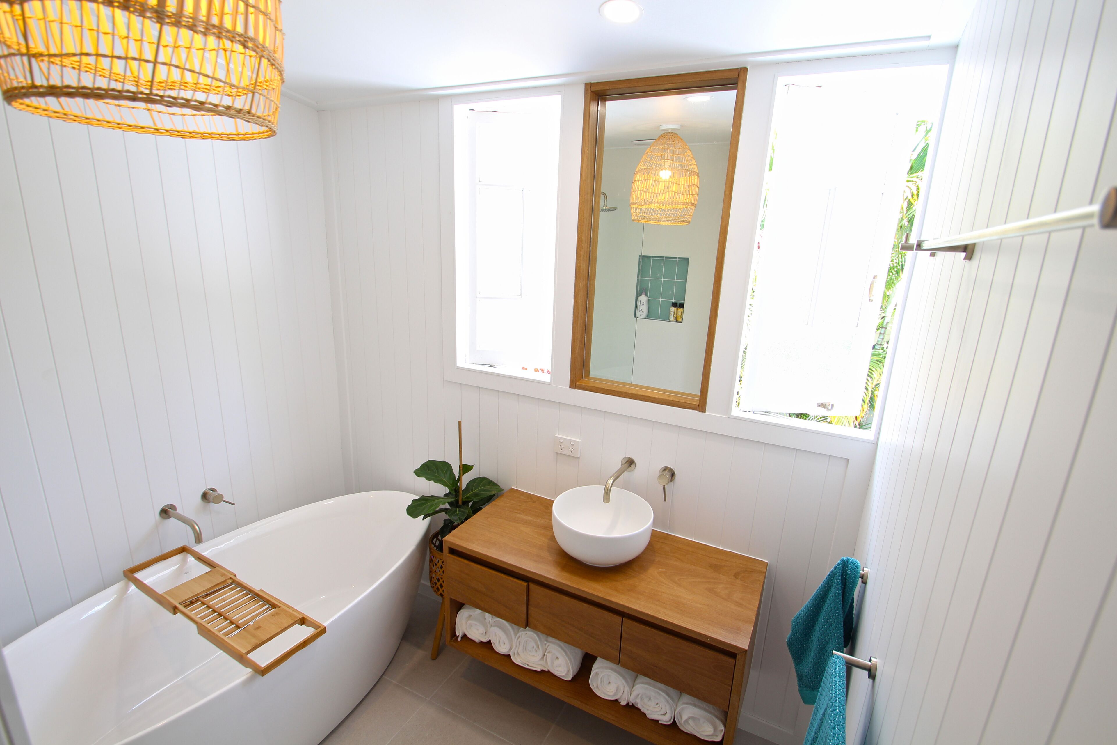 Une salle de bain avec une baignoire blanche, un meuble-lavabo en bois et une fenêtre donnant sur un paysage verdoyant.