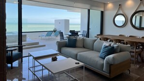 Una sala de estar moderna con un gran ventanal con vista al mar, un ventilador de techo y un comedor con muebles de madera.