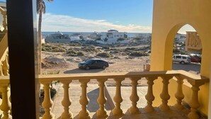Ein Balkon mit Blick auf eine Wüstenlandschaft, mit weißen Gebäuden und einem geparkten Auto.