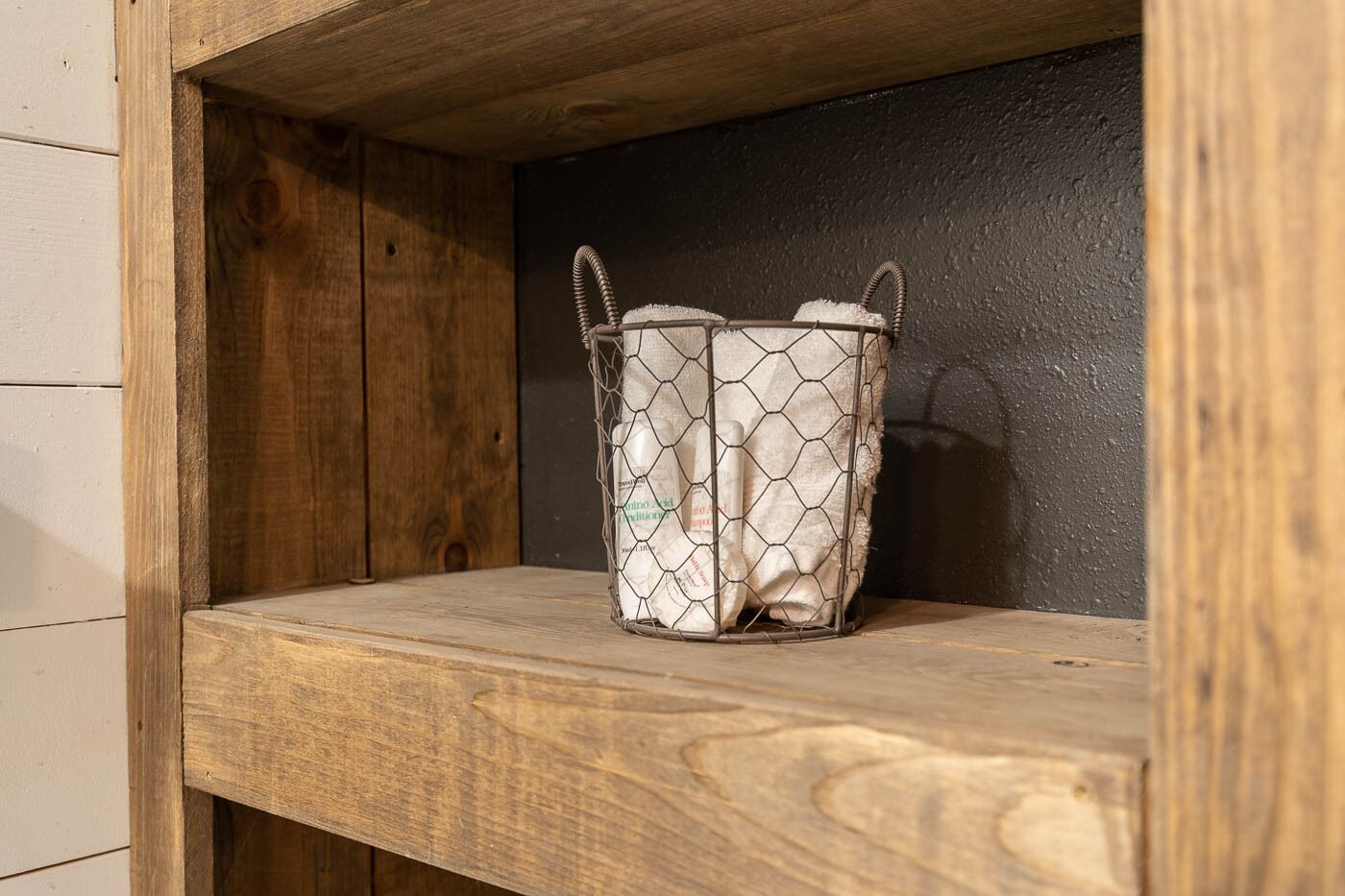 A wooden shelf with a wire basket containing a white bottle.