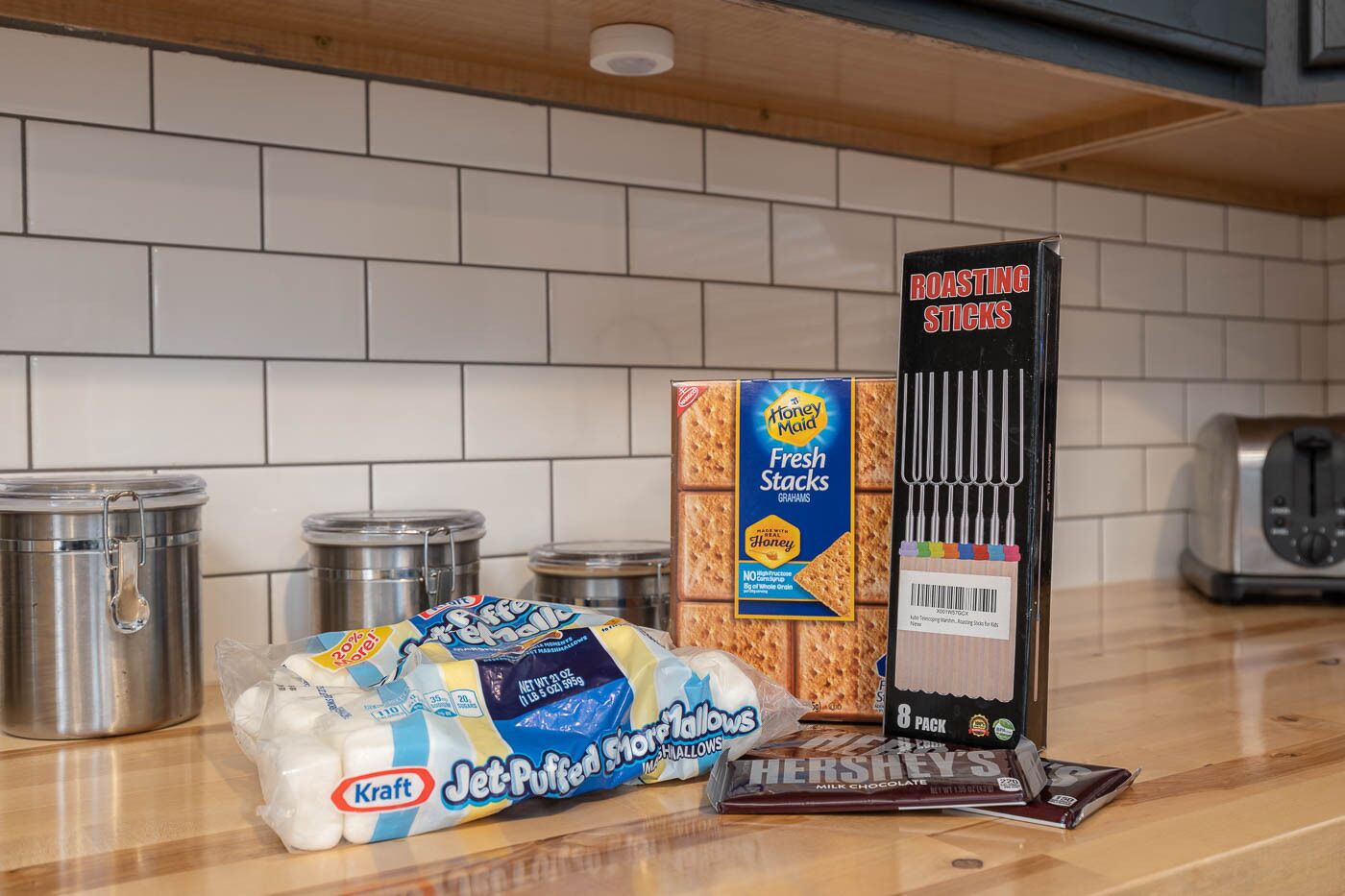 En köksbänk med Kraft Jet-Puffed marshmallows, Honey Maid Fresh Stacks-kex och en låda med spett för att grilla marshmallows.