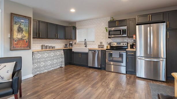 A modern kitchen with dark cabinets, stainless steel appliances, a white tiled backsplash, and a wooden floor. - Studied Perfection (Spearfish)
