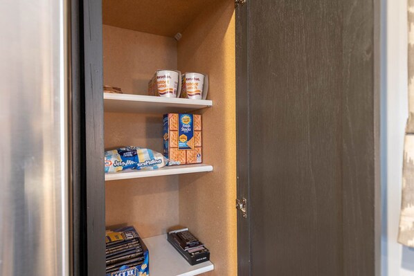 A pantry with shelves stocked with food items including jars, boxes of cereal, and snacks.