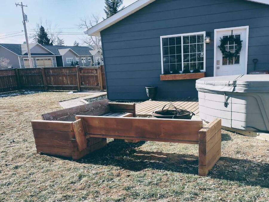 Een achtertuin met een houten bankje, een tuinhuisje en een jacuzzi.
