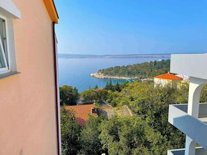 A balcony with a view of a coastal landscape, including a body of water and a hilly area with buildings.