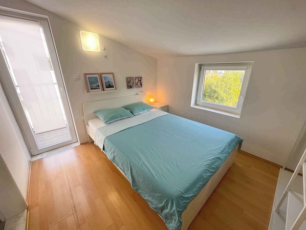A bedroom with a bed, a window, a door, and a wall-mounted light fixture.