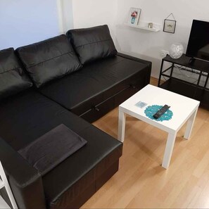 A modern living room with a black leather sofa, a white coffee table, and a TV on a stand.