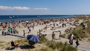 Una playa concurrida donde gente se toma el sol y pasea por la orilla.