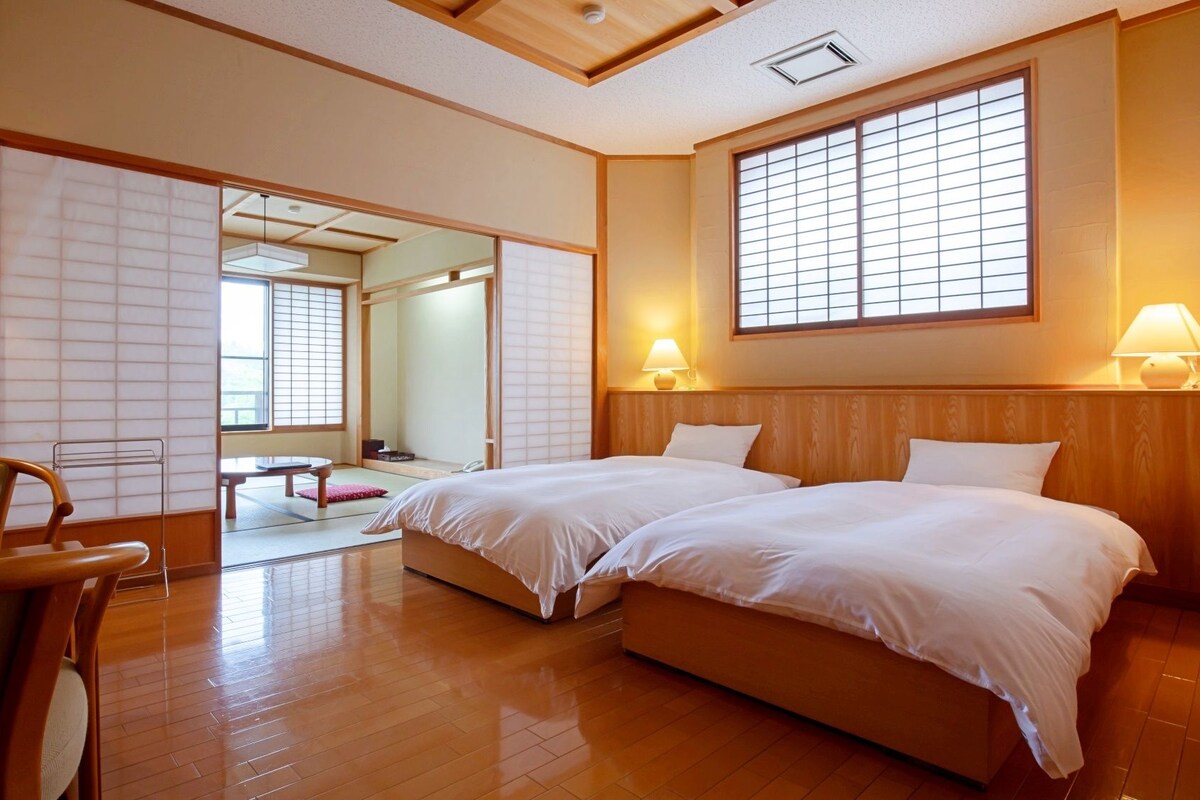 Habitación de hotel con dos camas, piso de madera, una silla y una puerta corredera que da a un baño.