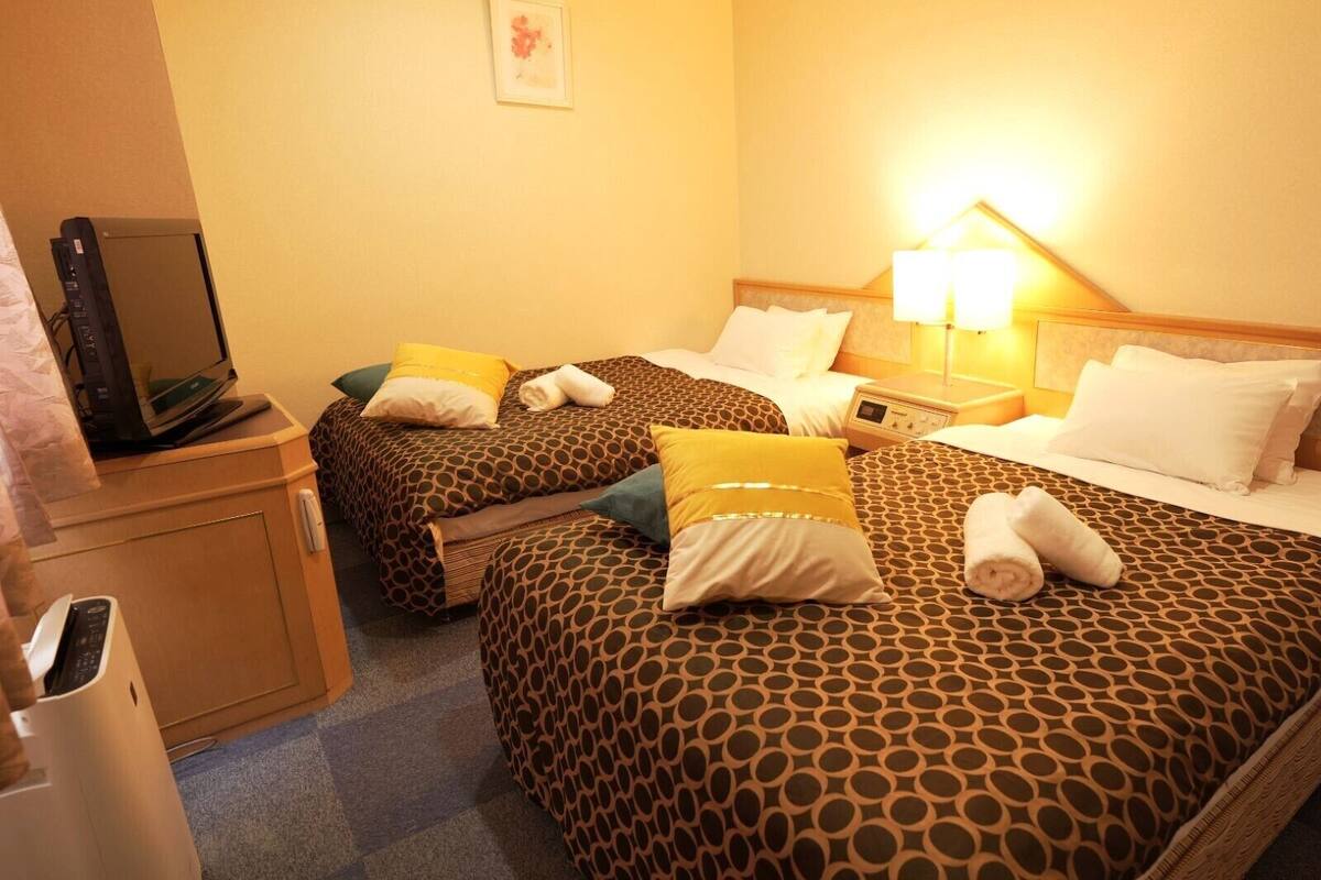 Una habitación de hotel con dos camas, un escritorio con ordenador y un cubo de basura.