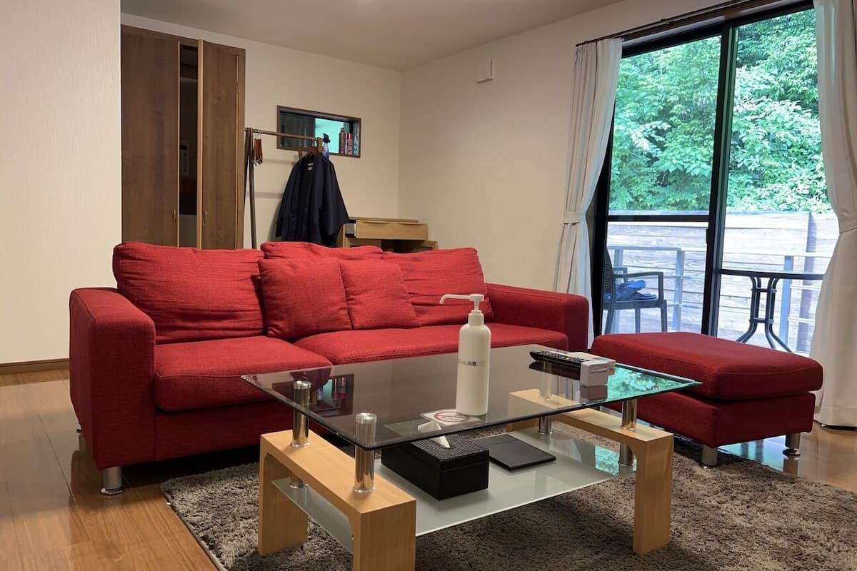 Un canapé rouge, une table basse en verre et un pouf rouge dans une pièce dotée d’une grande fenêtre et d’un plancher en bois.
