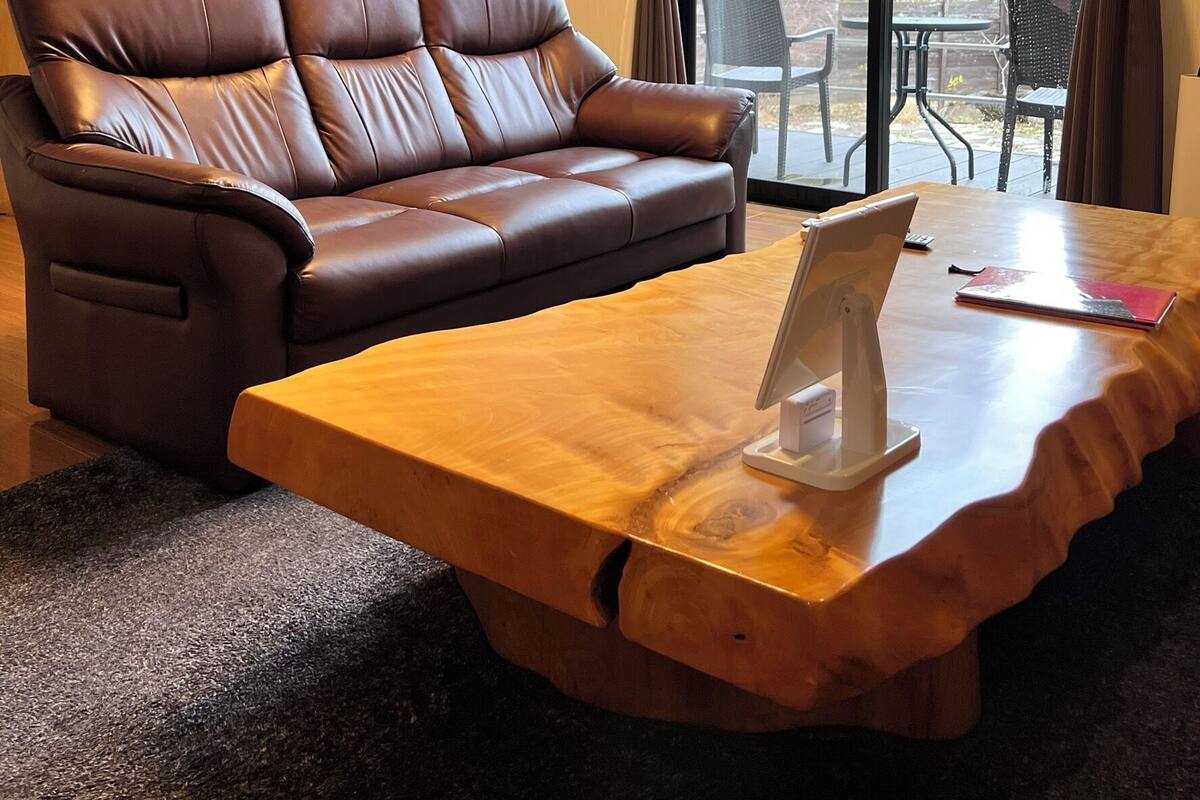 Une pièce avec un canapé en cuir marron, une table basse en bois et une vue sur des meubles d’extérieur, visible à travers une grande fenêtre.