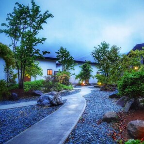 A pathway leading to a building with a traditional architectural style, surrounded by greenery and rocks. - Hanare Ohka (Yamaga)