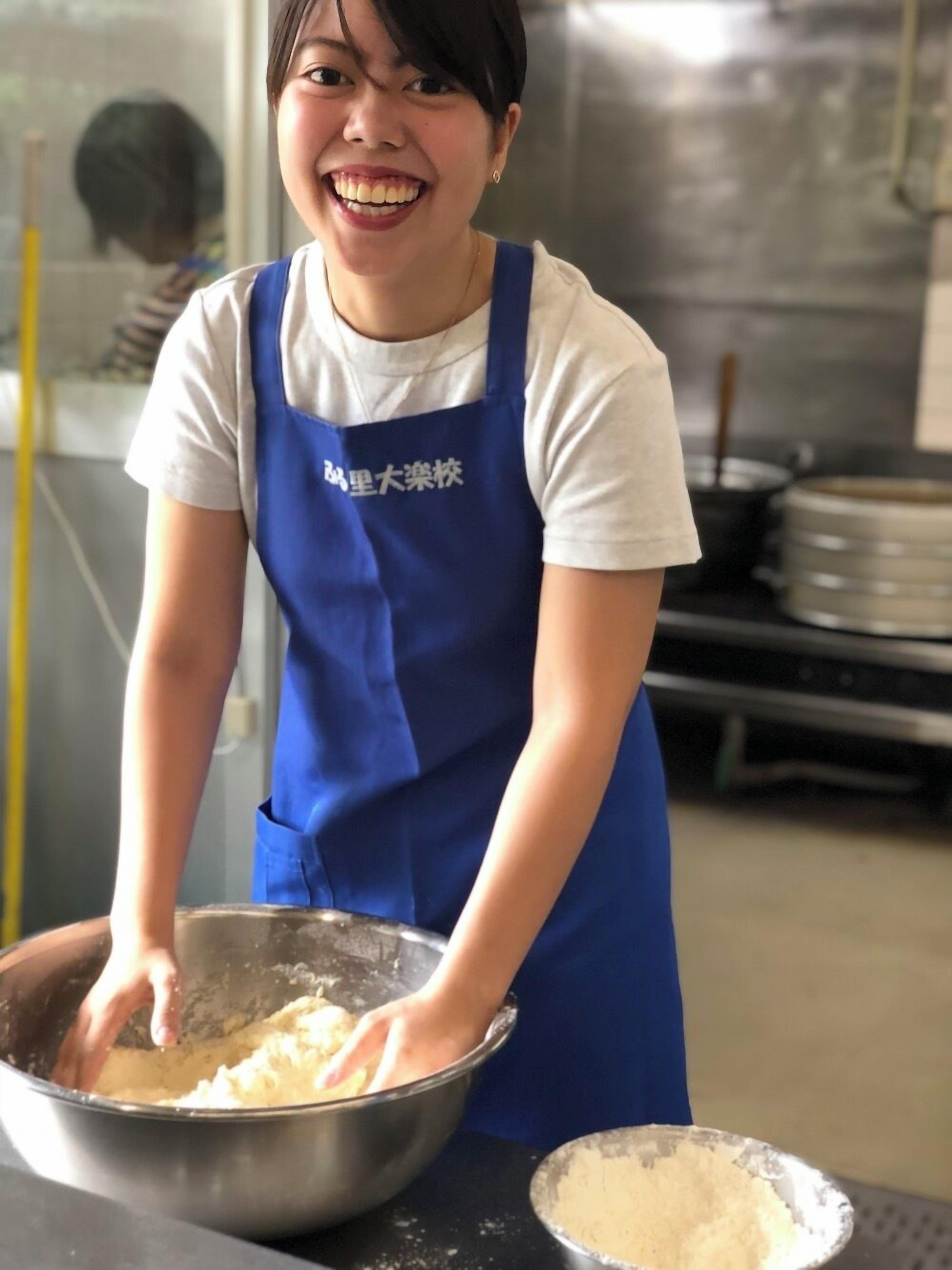 A person wearing a blue apron, mixing ingredients in a metal bowl.