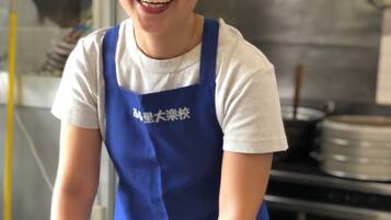 A person wearing a blue apron, mixing ingredients in a metal bowl.