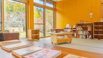 Uma biblioteca com grandes janelas, estantes de madeira e uma mesa central repleta de livros.