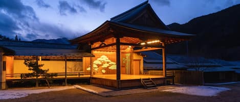 A traditional Japanese building with a wooden structure, a covered entrance, and a snow-covered landscape.
