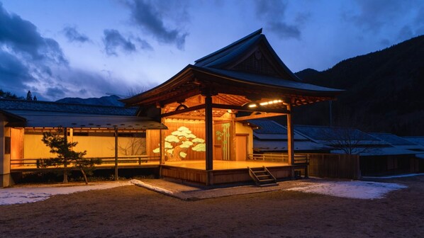 A traditional Japanese building with a wooden structure, a covered entrance, and a snow-covered landscape. - Green Village Yokokawa Kayabuki No Yakata (Tatsuno)
