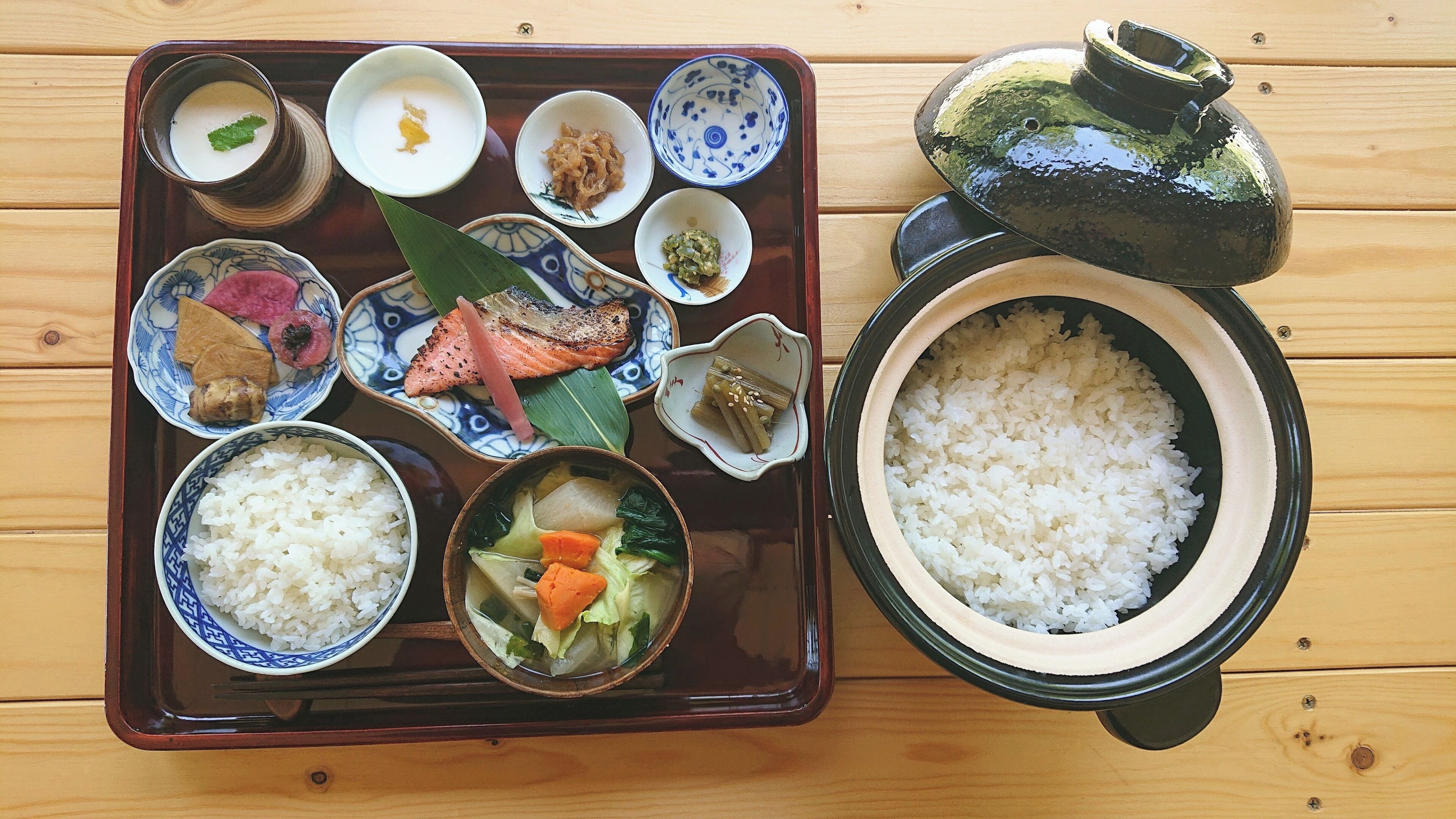 A traditional Japanese meal with rice, fish, and vegetables on a wooden tray.