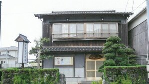 A traditional Japanese building with a wooden facade, large windows, and a stone pathway leading to the entrance. - Tomiya Kinbe-tei (Ozu)