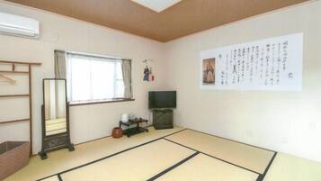 A traditional Japanese room with tatami flooring, a sliding door, a television, and a wall with calligraphy.