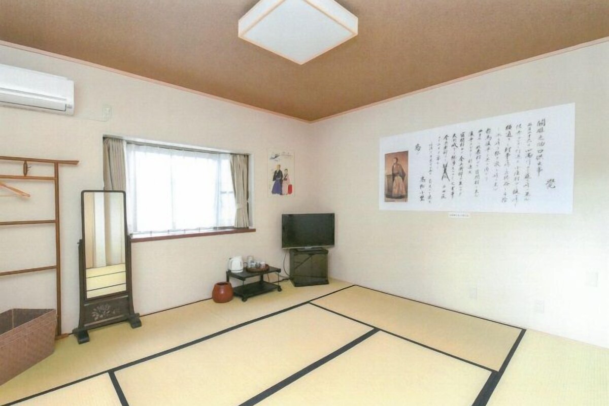Una habitació tradicional japonesa amb terra de tatami, una porta corredissa, una televisió i una paret amb cal·ligrafia.