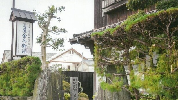 A traditional Japanese building with a stone gate, a wooden structure with a tiled roof, and a signboard with Japanese characters. - Tomiya Kinbe-tei (Ozu)