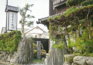Un bâtiment traditionnel japonais doté d’une porte en pierre, d’une structure en bois surmontée d’un toit en tuiles et d’une enseigne ornée de caractères japonais.